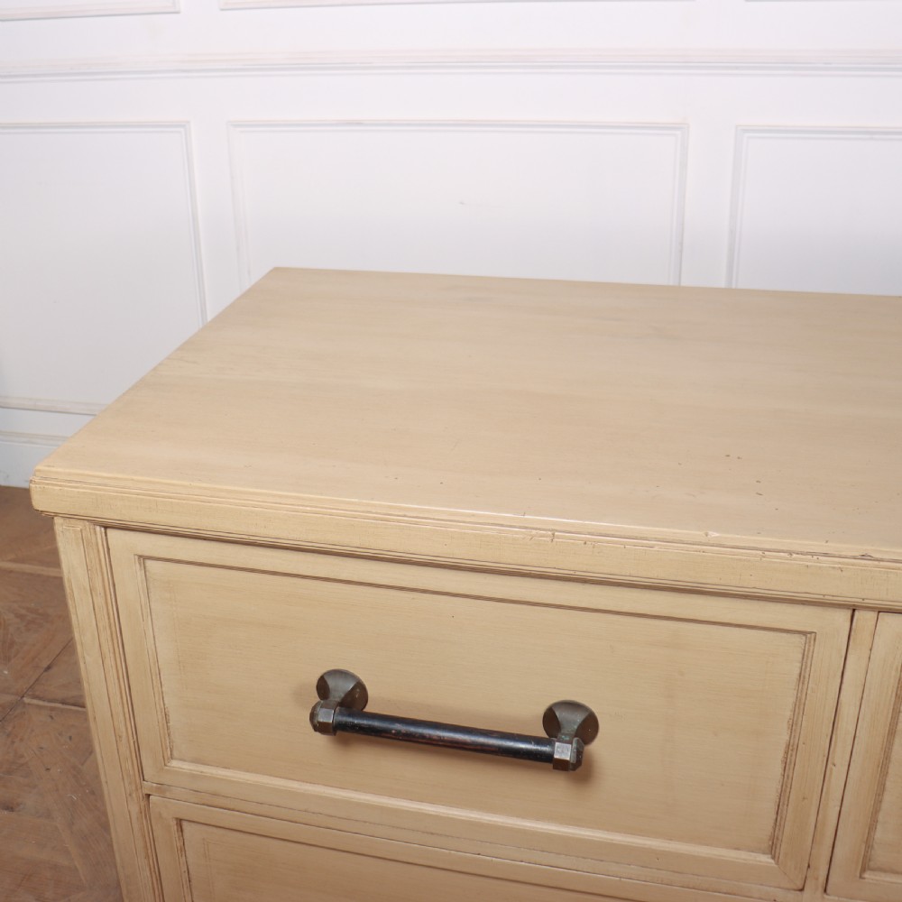 A low, wide wooden drapers chest in a neutral beige painted finish featuring four large paneled drawers with dark metal handles. View VIII