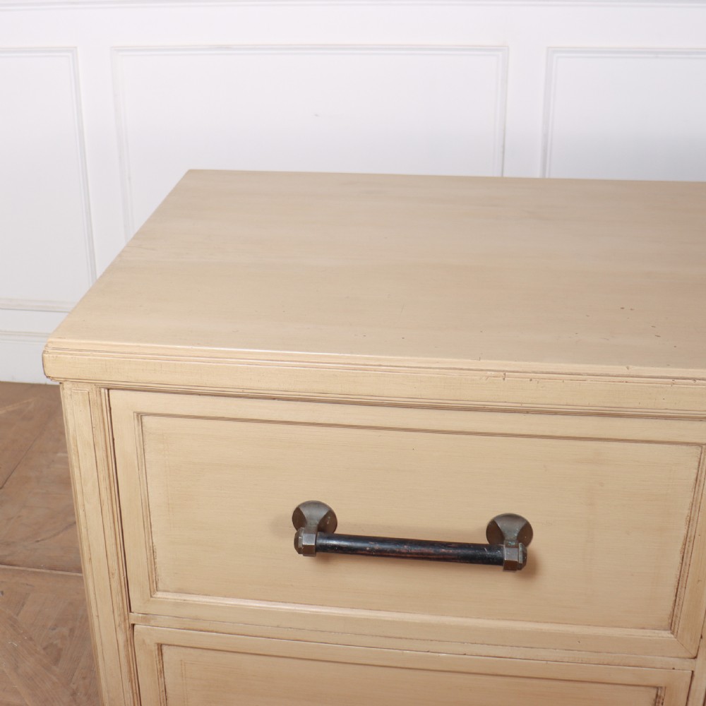 A low, wide wooden drapers chest in a neutral beige painted finish featuring four large paneled drawers with dark metal handles. View IX