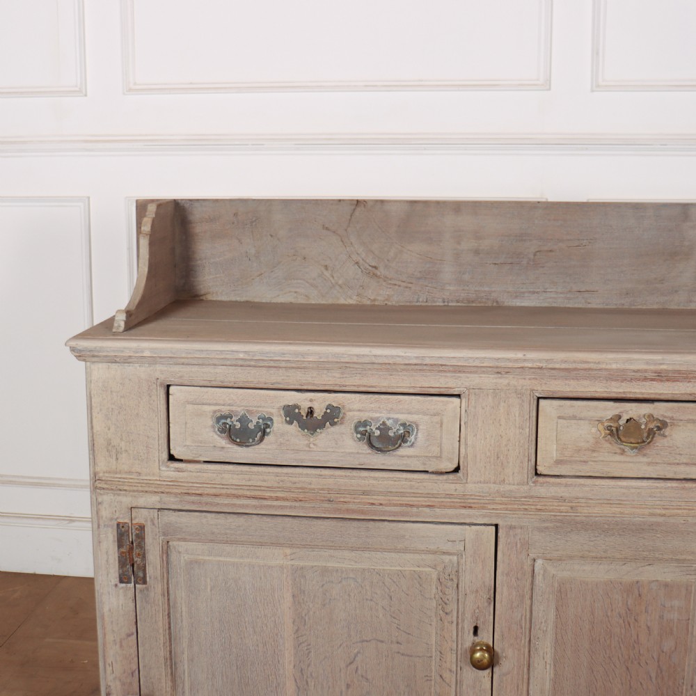 An 18th-century bleached oak dresser base featuring three top drawers, panelled cupboard doors, and a simple low wooden gallery back. View II