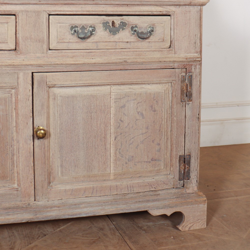An 18th-century bleached oak dresser base featuring three top drawers, panelled cupboard doors, and a simple low wooden gallery back. View III