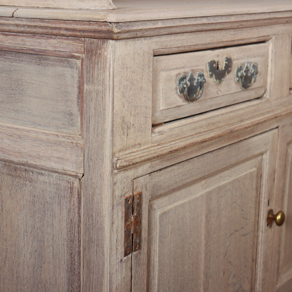 An 18th-century bleached oak dresser base featuring three top drawers, panelled cupboard doors, and a simple low wooden gallery back. View VIII