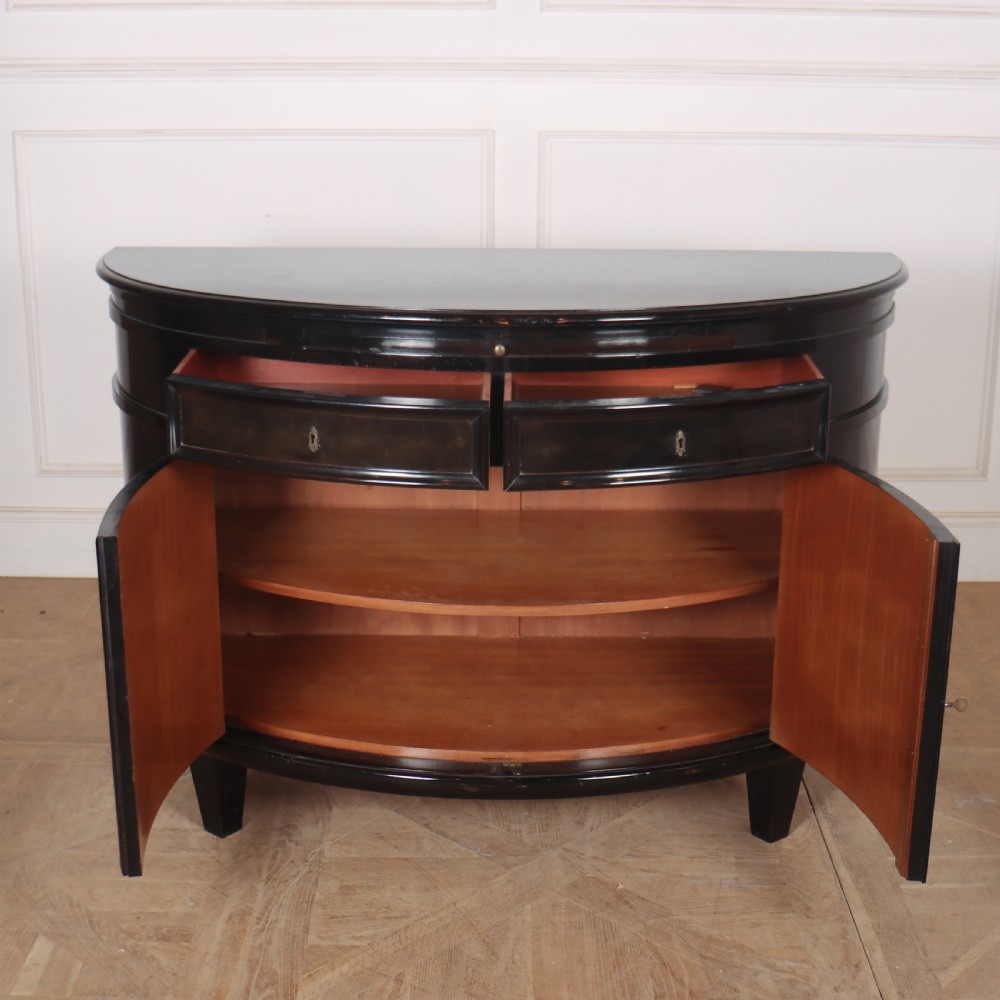 A French ebonised demi lune cabinet featuring a semi-circular body, top drawers with keyhole escutcheons, panelled cupboard doors, and square tapered feet. View III