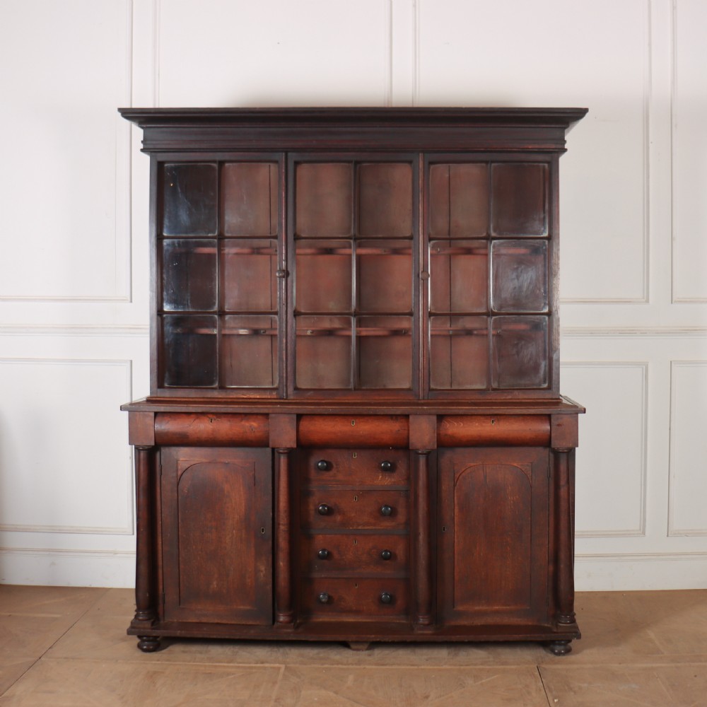A dark brown antique oak glazed dresser featuring a upper display cabinet with three glass-front doors above a base with drawers and cupboard doors.