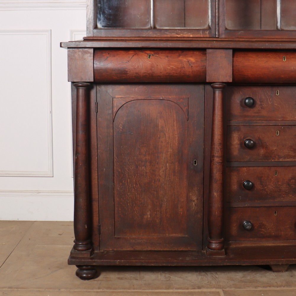 A dark brown antique oak glazed dresser featuring a upper display cabinet with three glass-front doors above a base with drawers and cupboard doors. View II