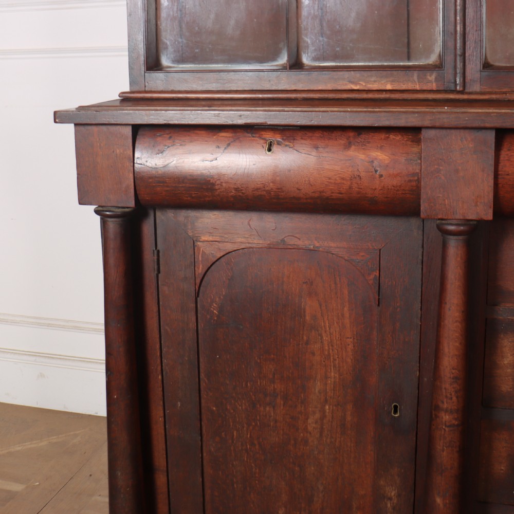A dark brown antique oak glazed dresser featuring a upper display cabinet with three glass-front doors above a base with drawers and cupboard doors. View III
