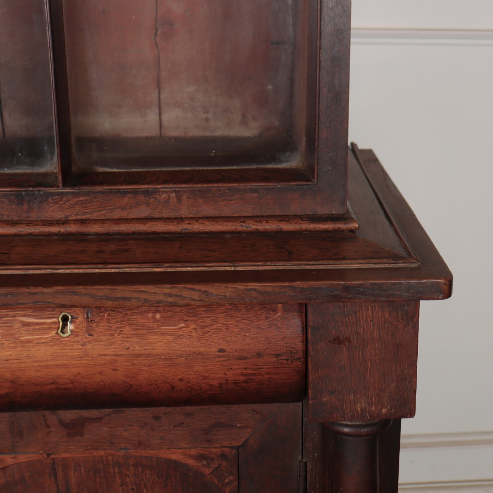 A dark brown antique oak glazed dresser featuring a upper display cabinet with three glass-front doors above a base with drawers and cupboard doors. View VI