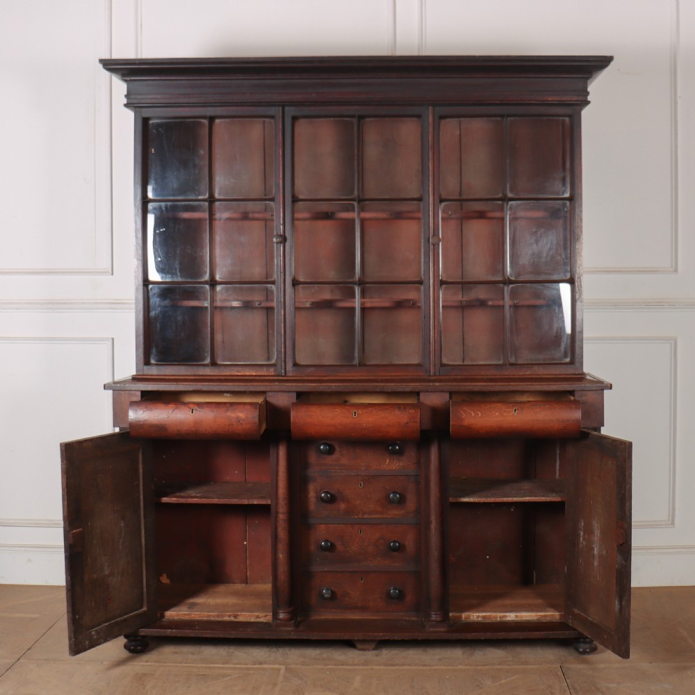 A dark brown antique oak glazed dresser featuring a upper display cabinet with three glass-front doors above a base with drawers and cupboard doors. View VII
