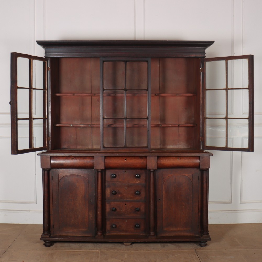 A dark brown antique oak glazed dresser featuring a upper display cabinet with three glass-front doors above a base with drawers and cupboard doors. View IX