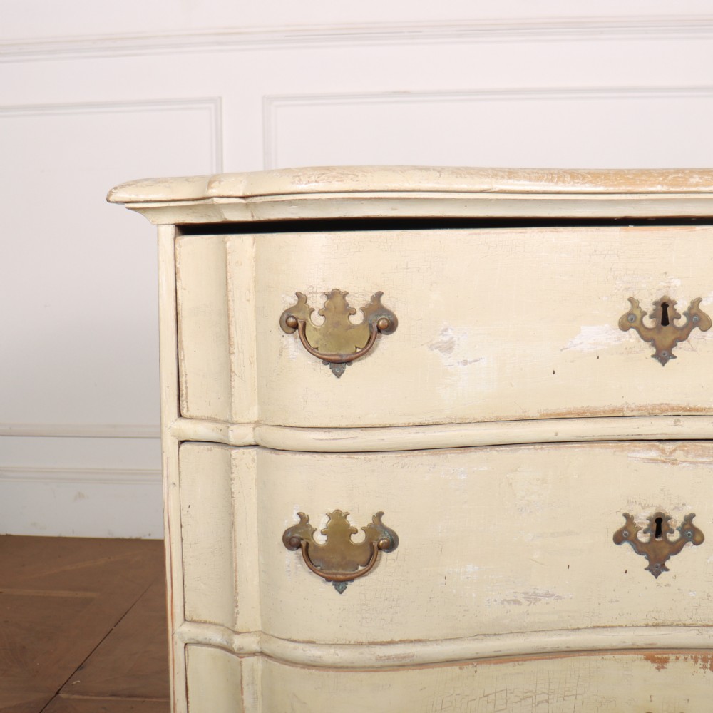 An 18th-century serpentine commode featuring three drawers with a distressed cream paint finish and cast brass hardware. View II