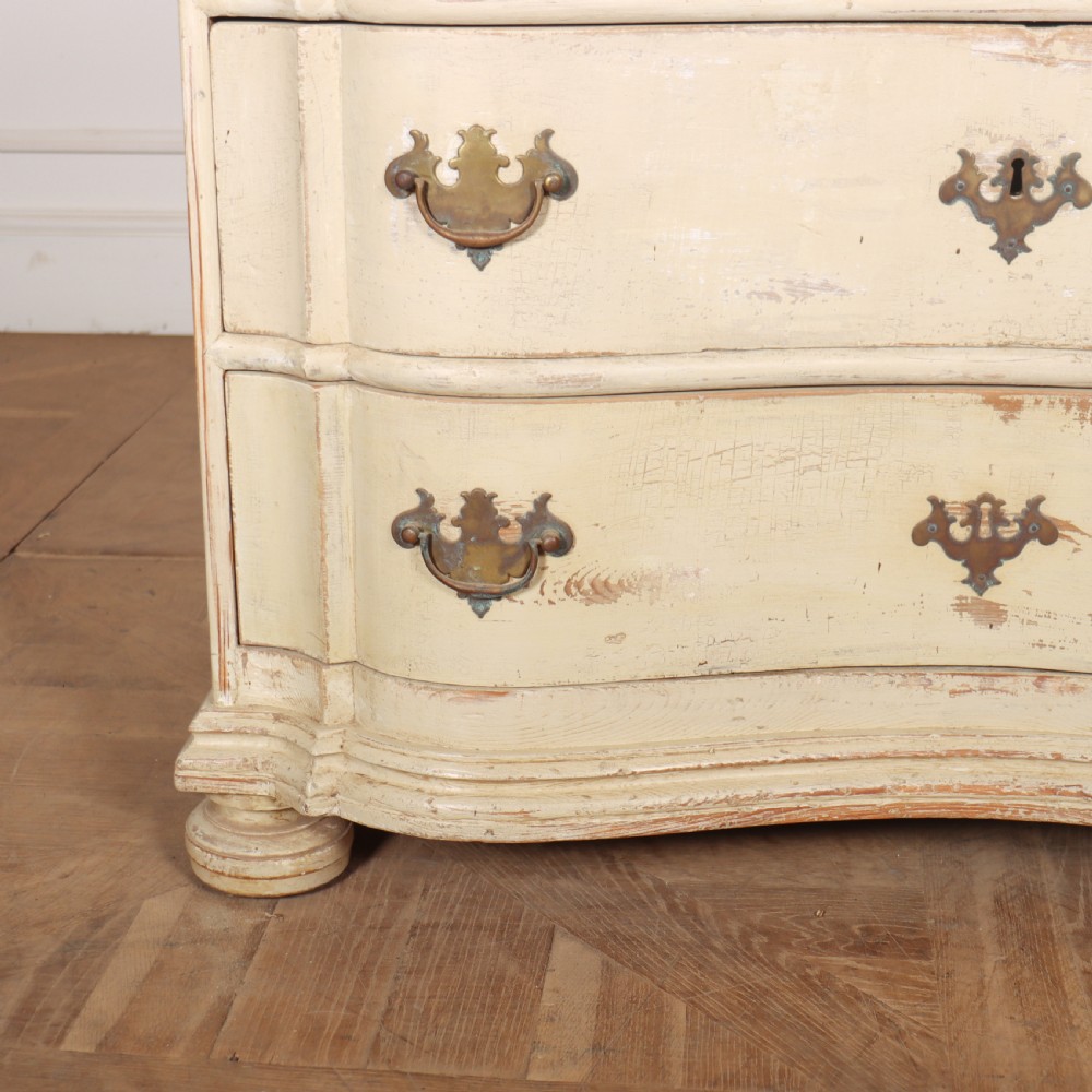 An 18th-century serpentine commode featuring three drawers with a distressed cream paint finish and cast brass hardware. View III