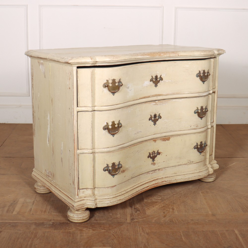 An 18th-century serpentine commode featuring three drawers with a distressed cream paint finish and cast brass hardware. View VIII