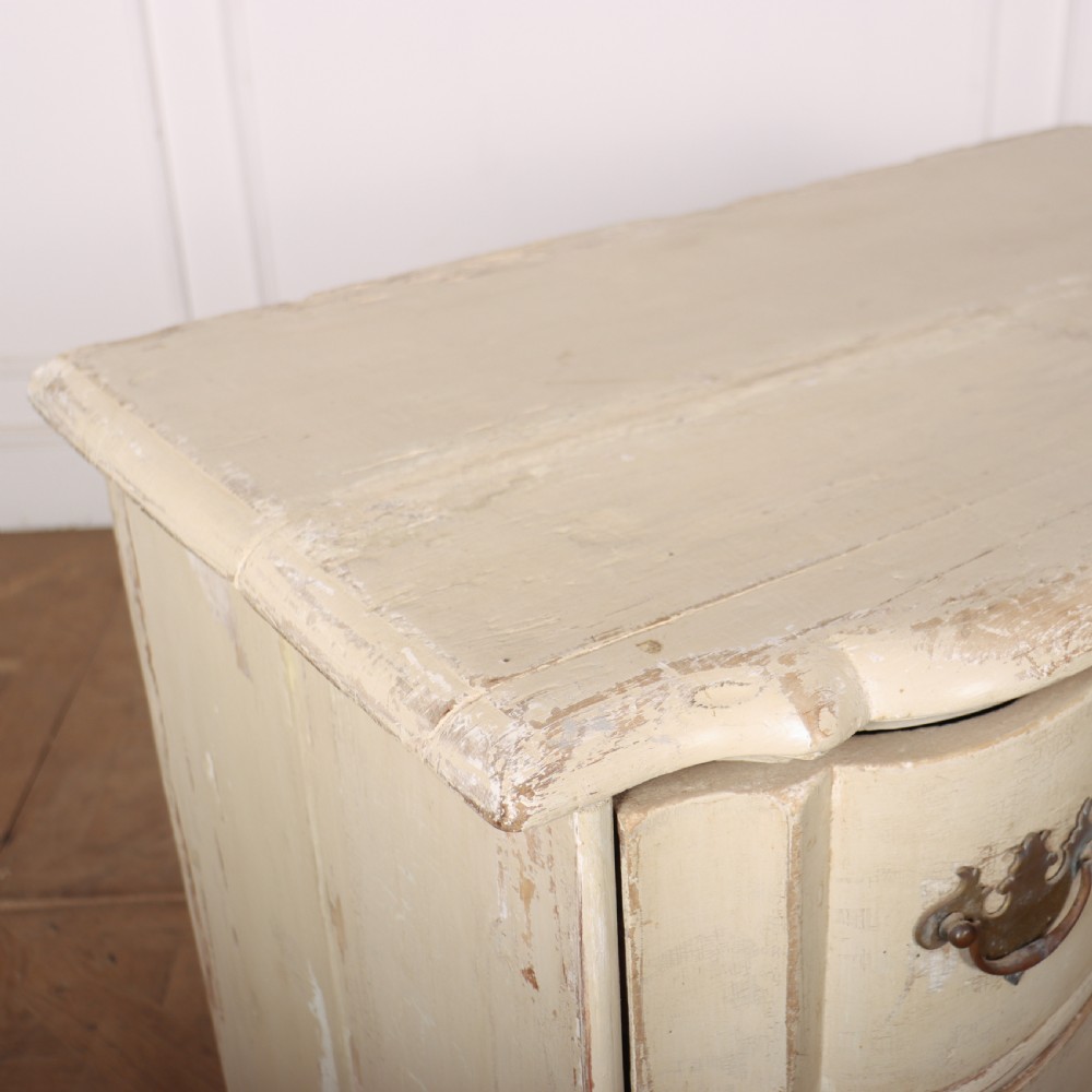 An 18th-century serpentine commode featuring three drawers with a distressed cream paint finish and cast brass hardware. View IX