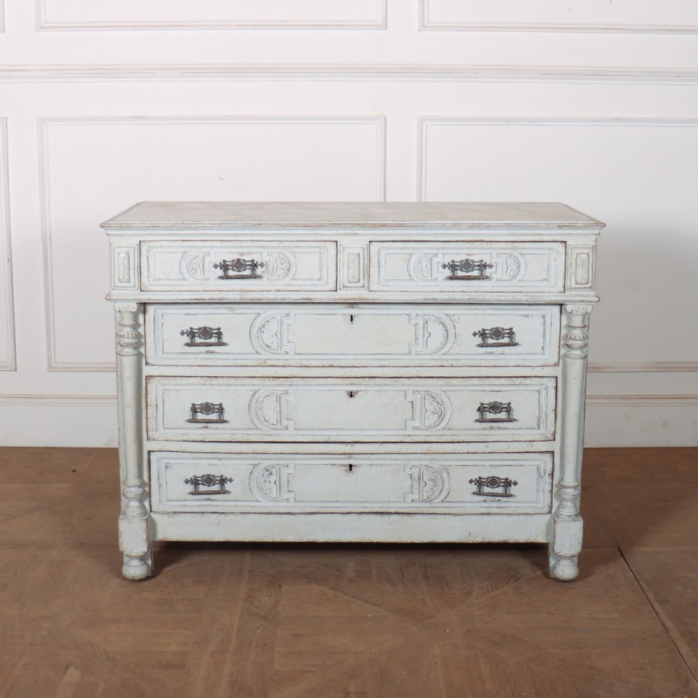 A pale grey painted antique French commode featuring carved drawer fronts, brass hardware, and turned fluted corner columns.