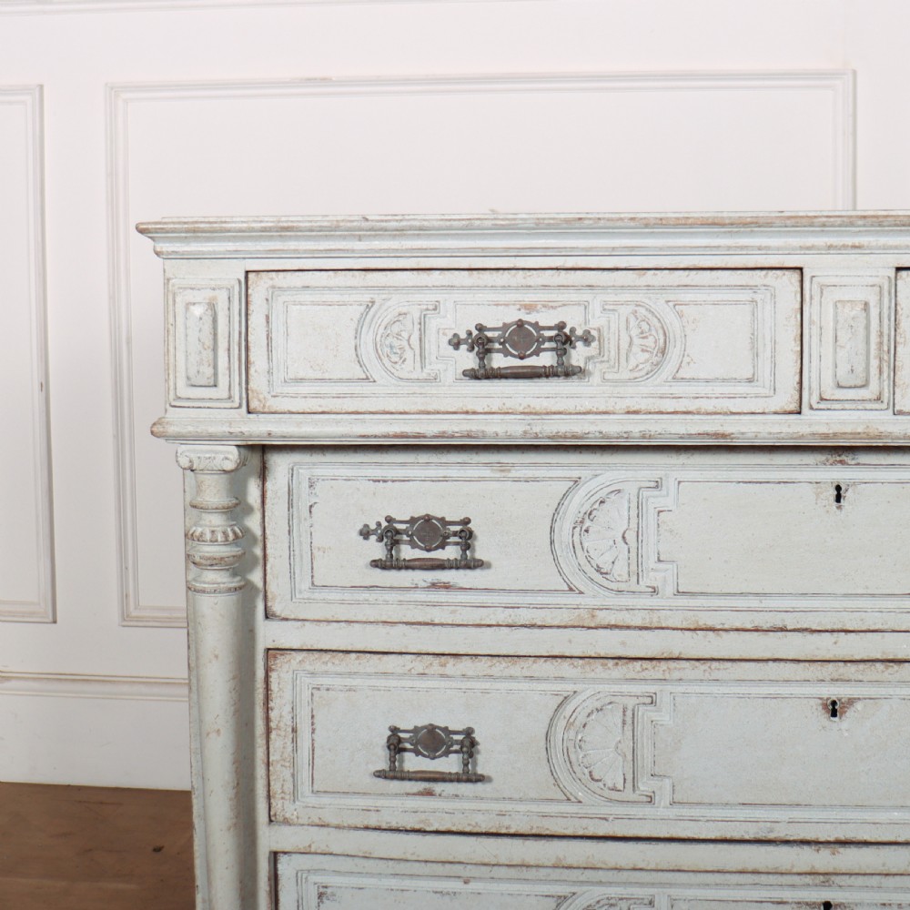 A pale grey painted antique French commode featuring carved drawer fronts, brass hardware, and turned fluted corner columns. View II