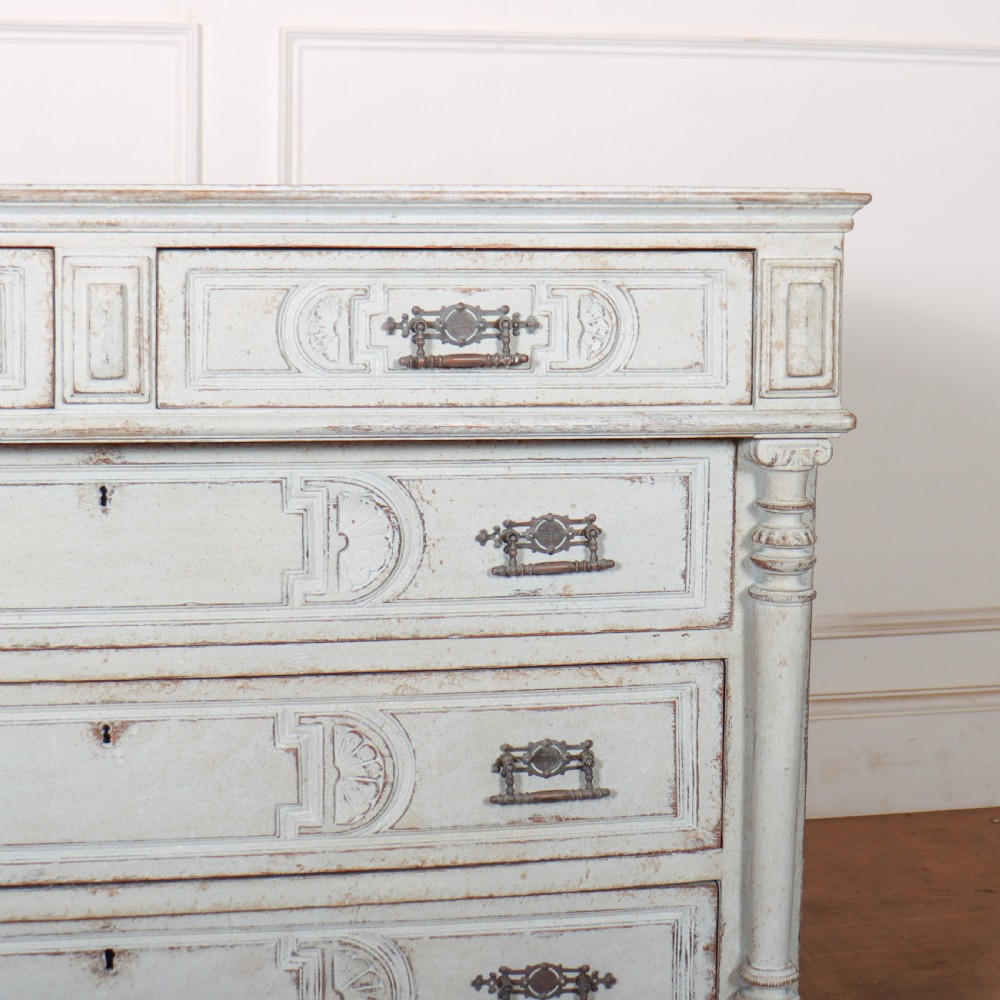 A pale grey painted antique French commode featuring carved drawer fronts, brass hardware, and turned fluted corner columns. View VI