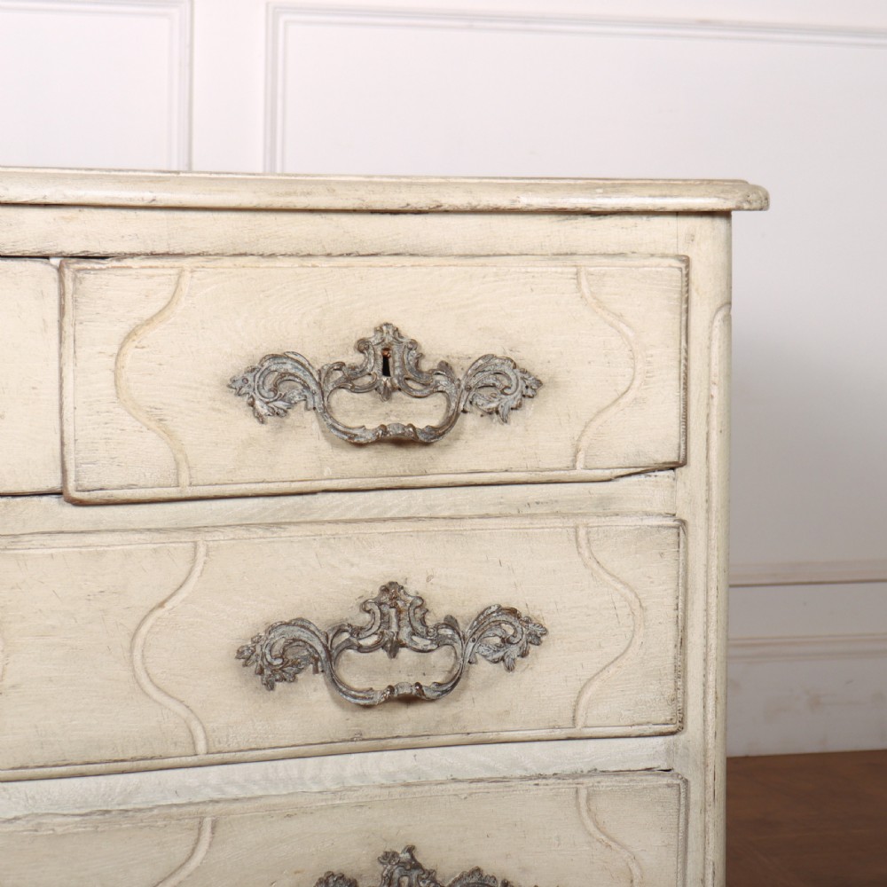 A French painted serpentine commode with three drawers, moulded panels, ornate brass handles, and short cabriole legs. View V