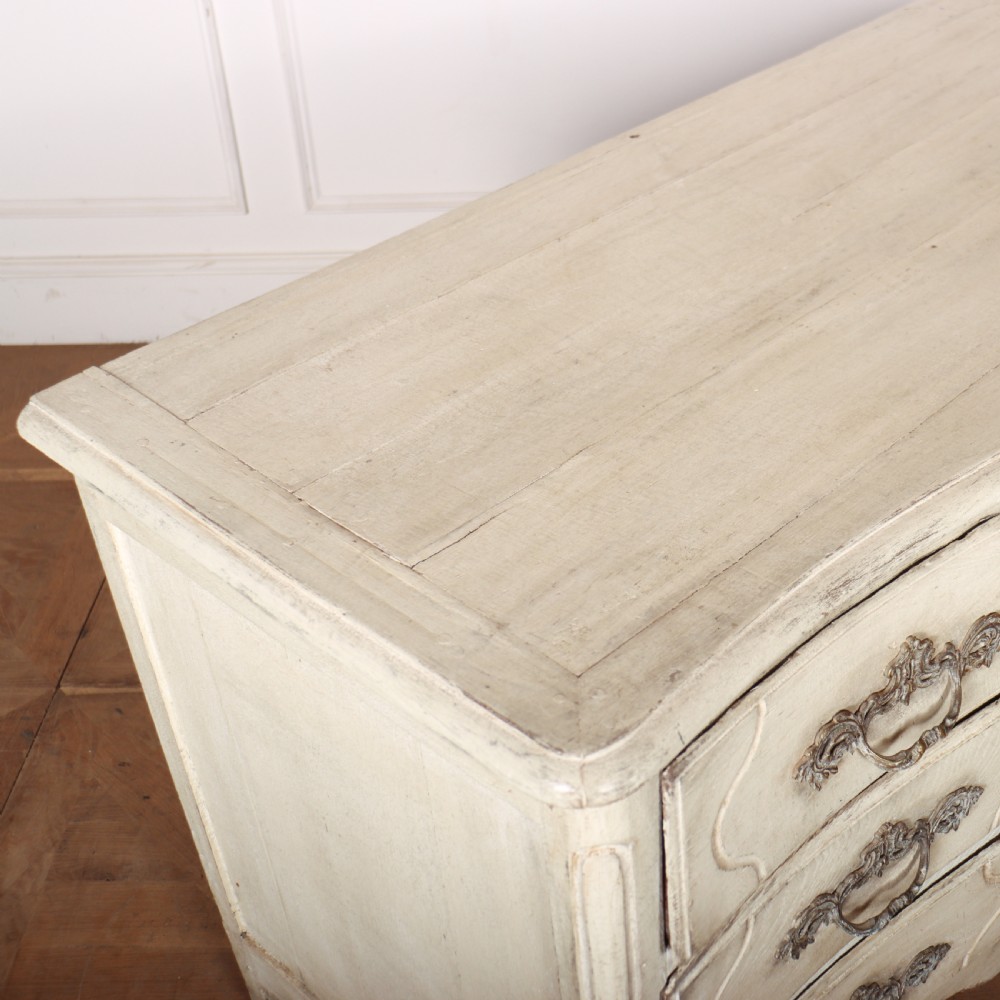 A French painted serpentine commode with three drawers, moulded panels, ornate brass handles, and short cabriole legs. View VIII