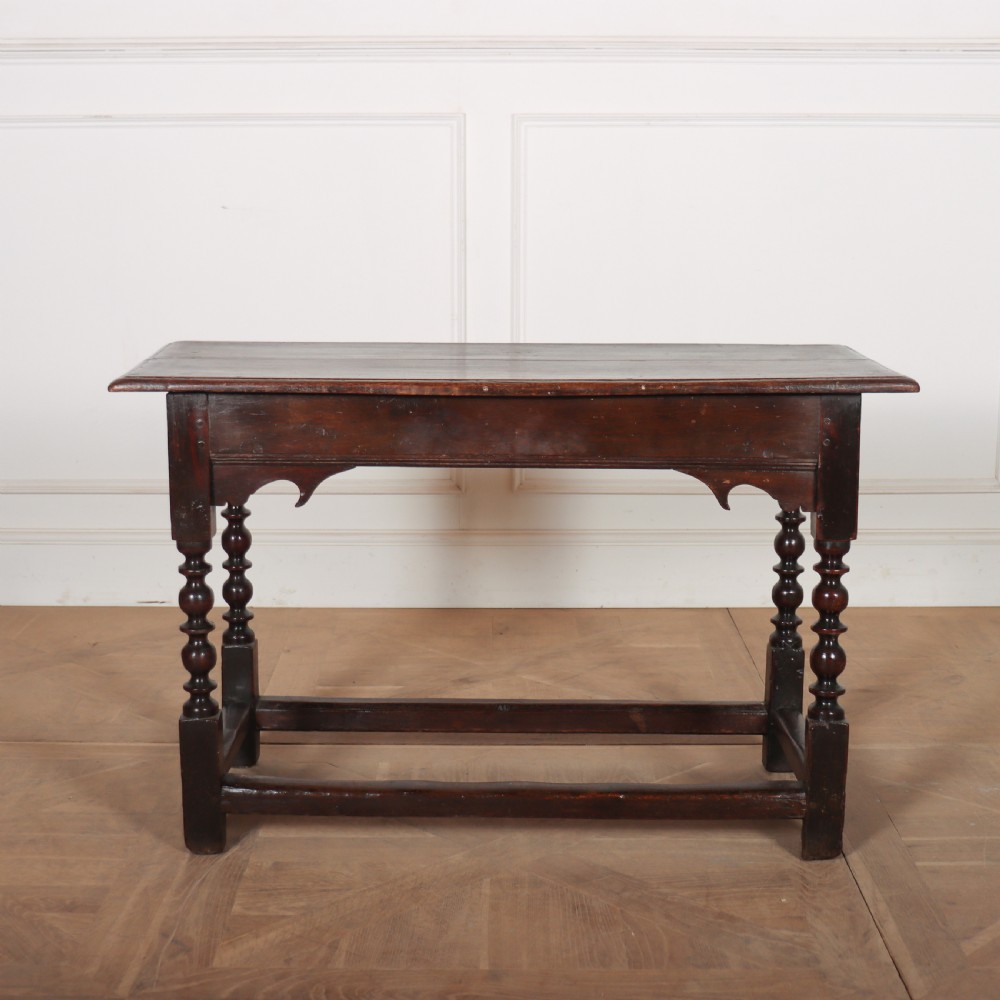 An 18th-century dark oak side table with turned legs, shaped apron, and perimeter stretcher base against a light background.