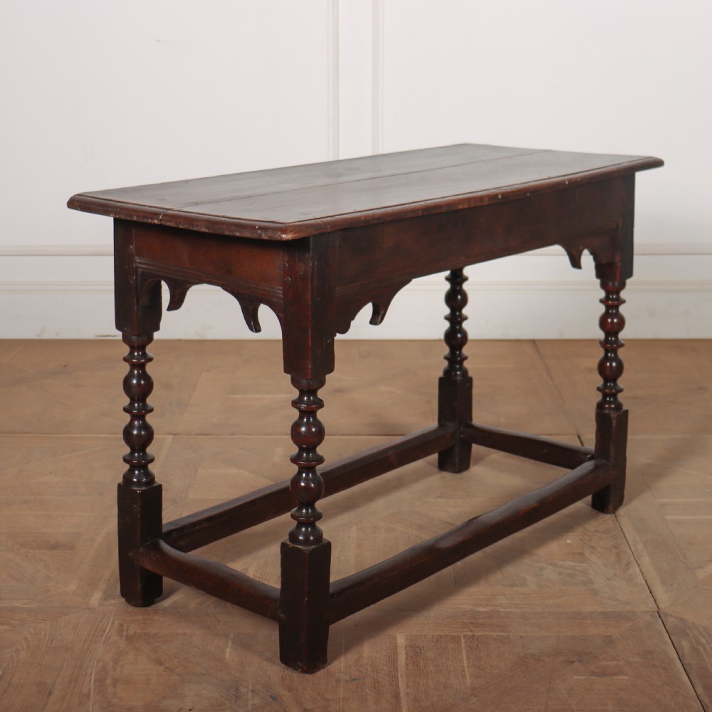 An 18th-century dark oak side table with turned legs, shaped apron, and perimeter stretcher base against a light background. View V