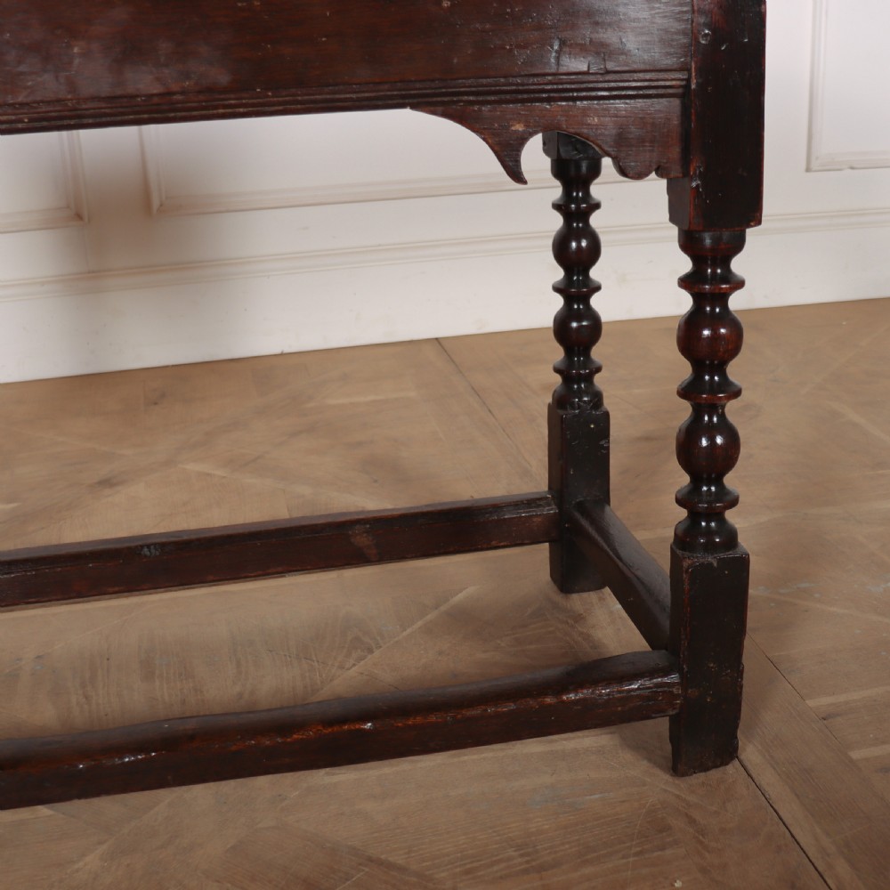 An 18th-century dark oak side table with turned legs, shaped apron, and perimeter stretcher base against a light background. View VI