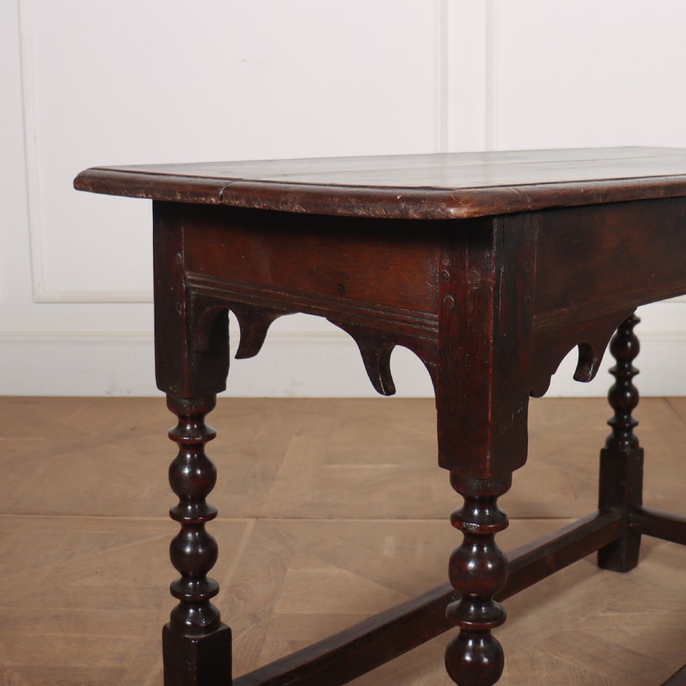 An 18th-century dark oak side table with turned legs, shaped apron, and perimeter stretcher base against a light background. View VIII