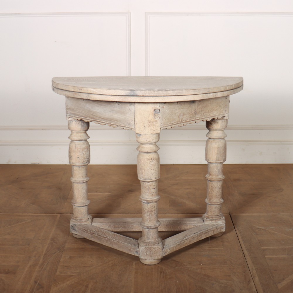 An 18th century Dutch demilune console table made from bleached oak, featuring three heavy turned legs, a scalloped apron, and a triangular low stretcher base.