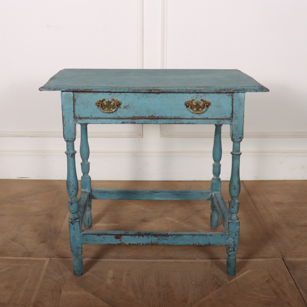 An 18th-century rectangular lamp table featuring a distressed blue painted finish, turned legs, a lower stretcher base, and a single drawer with brass handles.