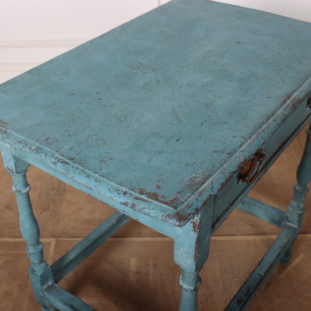 An 18th-century rectangular lamp table featuring a distressed blue painted finish, turned legs, a lower stretcher base, and a single drawer with brass handles. View VI