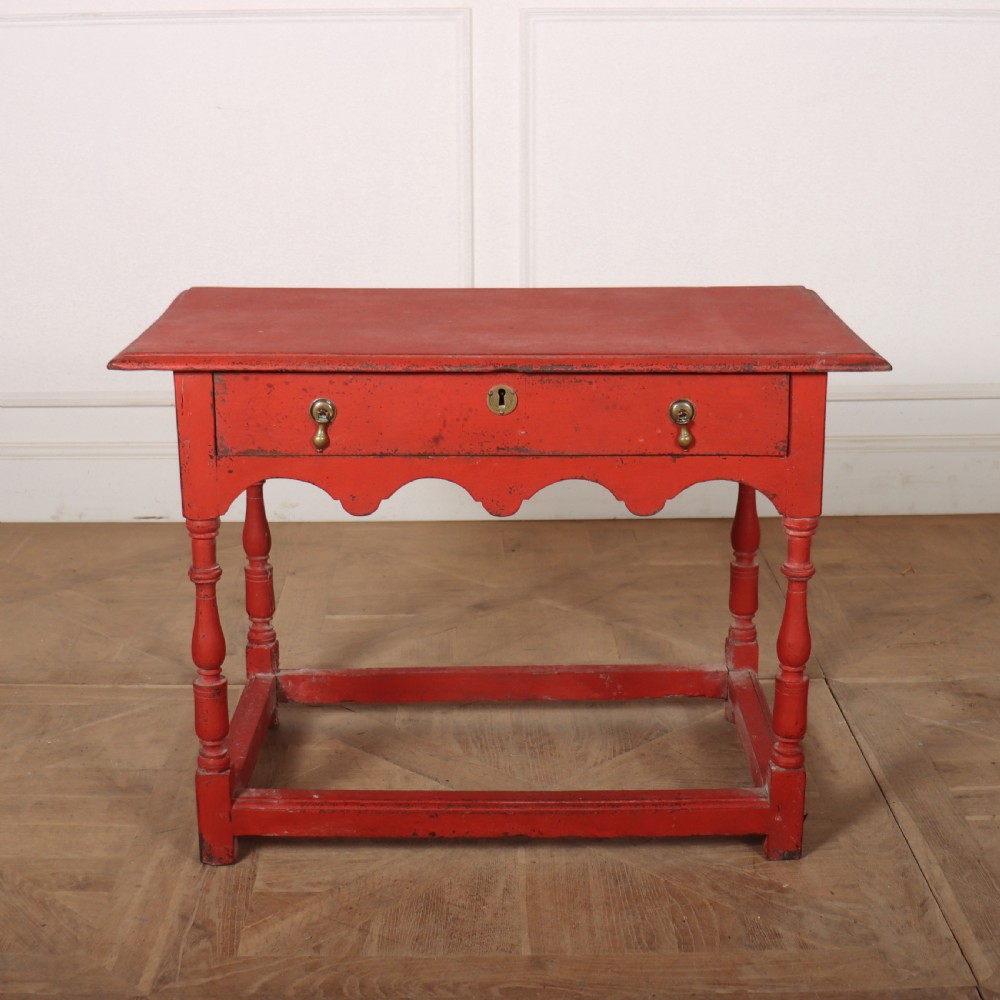 An 18th-century red painted timber side table featuring a single drawer with brass drop handles, a scalloped apron, turned legs, and a full box stretcher.
