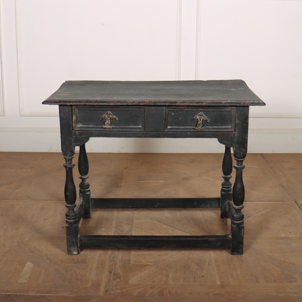 A distressed black painted wooden side table featuring two front drawers with brass handles, turned legs, and a low box stretcher.
