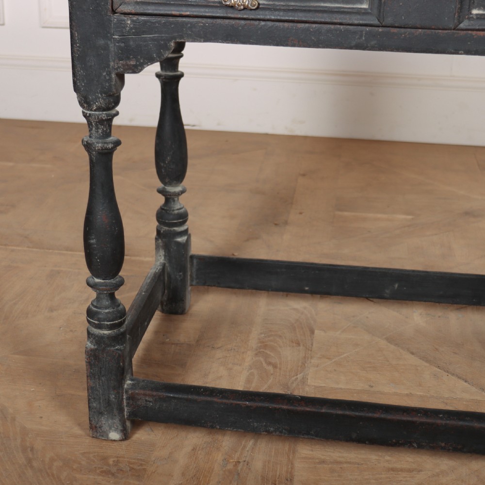 A distressed black painted wooden side table featuring two front drawers with brass handles, turned legs, and a low box stretcher. View III