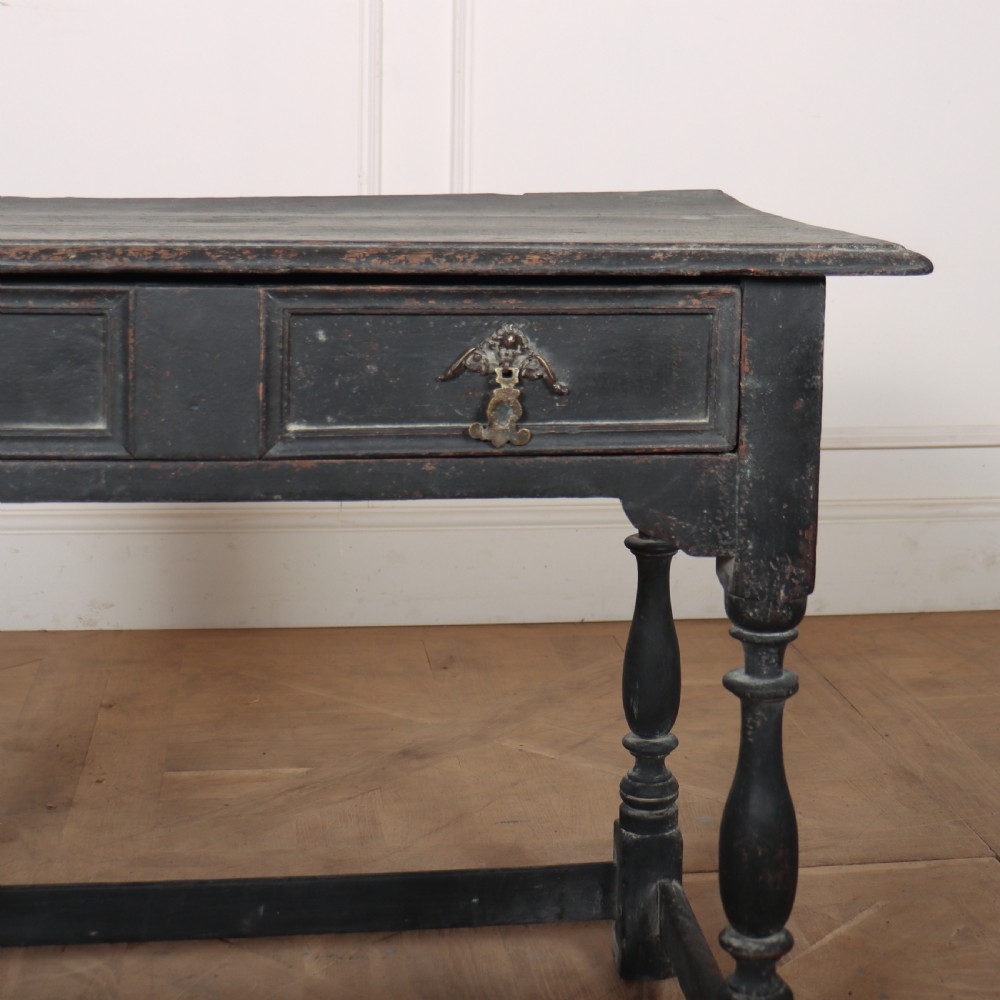 A distressed black painted wooden side table featuring two front drawers with brass handles, turned legs, and a low box stretcher. View V