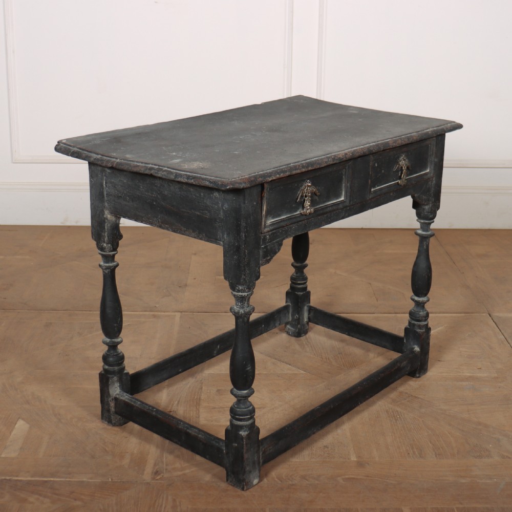 A distressed black painted wooden side table featuring two front drawers with brass handles, turned legs, and a low box stretcher. View VI