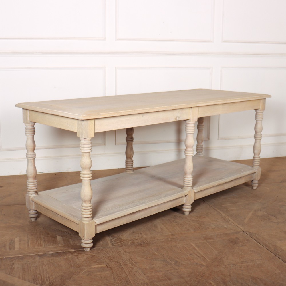 A long bleached oak French drapers table featuring six turned legs and a full-length lower tier shelf.