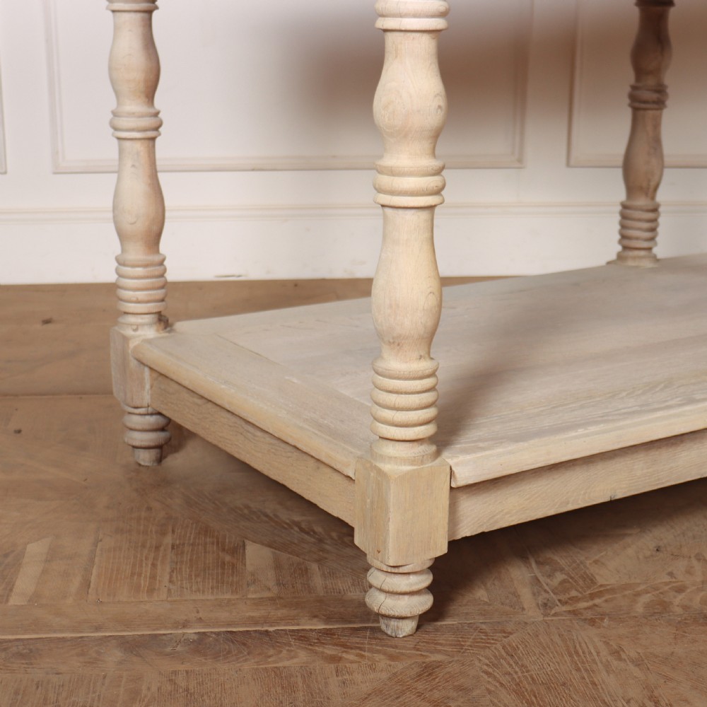 A long bleached oak French drapers table featuring six turned legs and a full-length lower tier shelf. View II