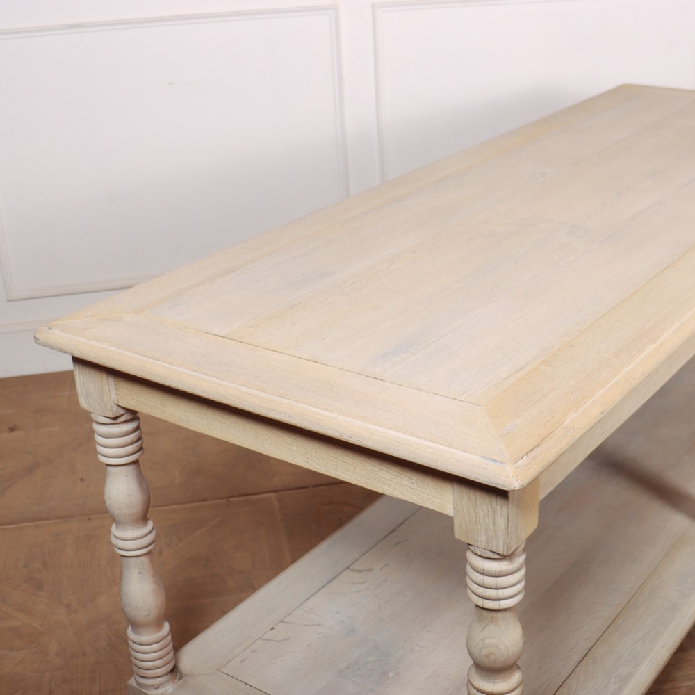 A long bleached oak French drapers table featuring six turned legs and a full-length lower tier shelf. View V