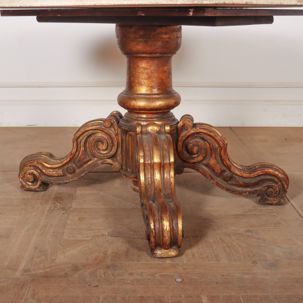 An antique circular table featuring a cream marble top resting upon a heavily carved giltwood pedestal base with four scroll feet. View II