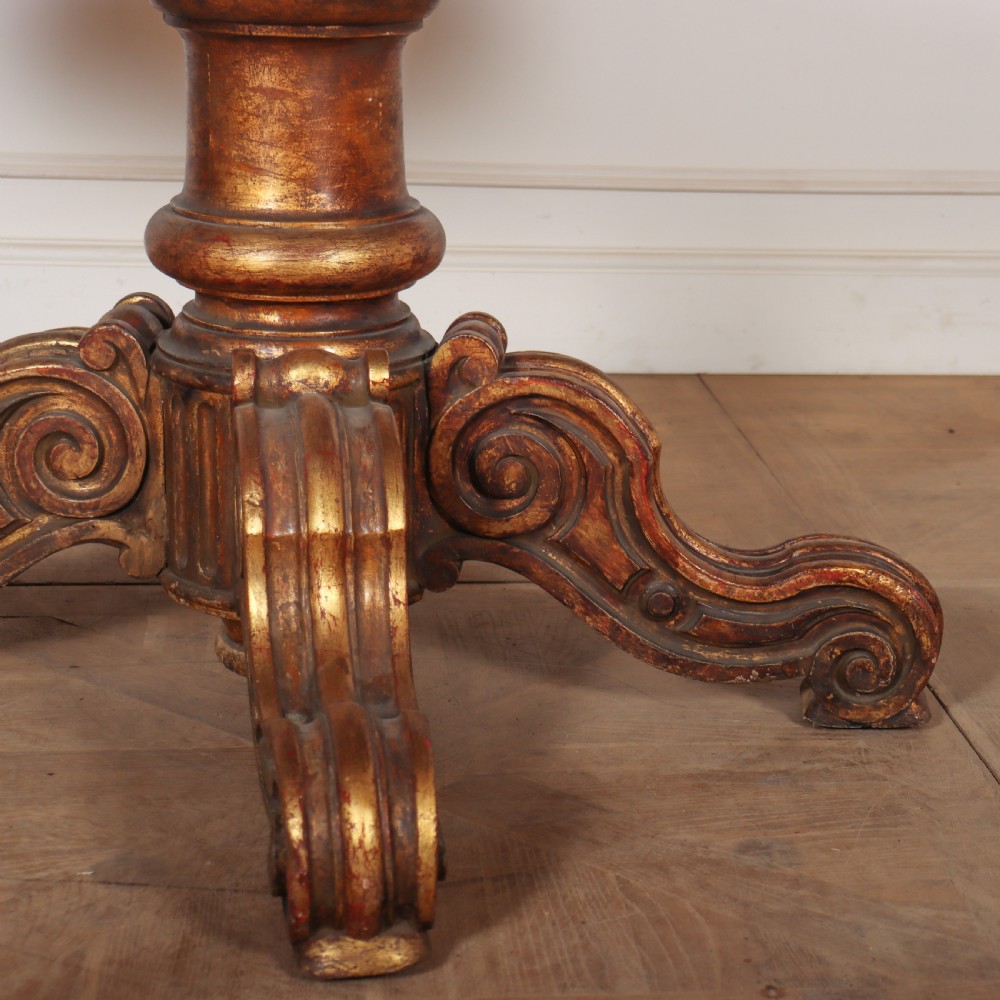 An antique circular table featuring a cream marble top resting upon a heavily carved giltwood pedestal base with four scroll feet. View III