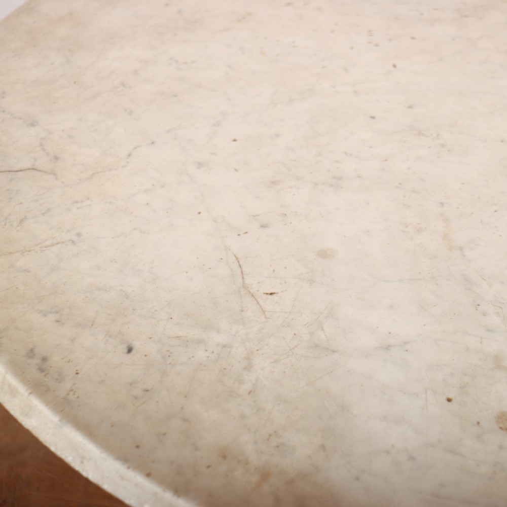 An antique circular table featuring a cream marble top resting upon a heavily carved giltwood pedestal base with four scroll feet. View V