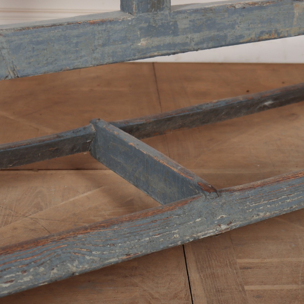 A long antique wooden tavern table with a natural wood plank top and a blue-painted X-frame trestle base. View II