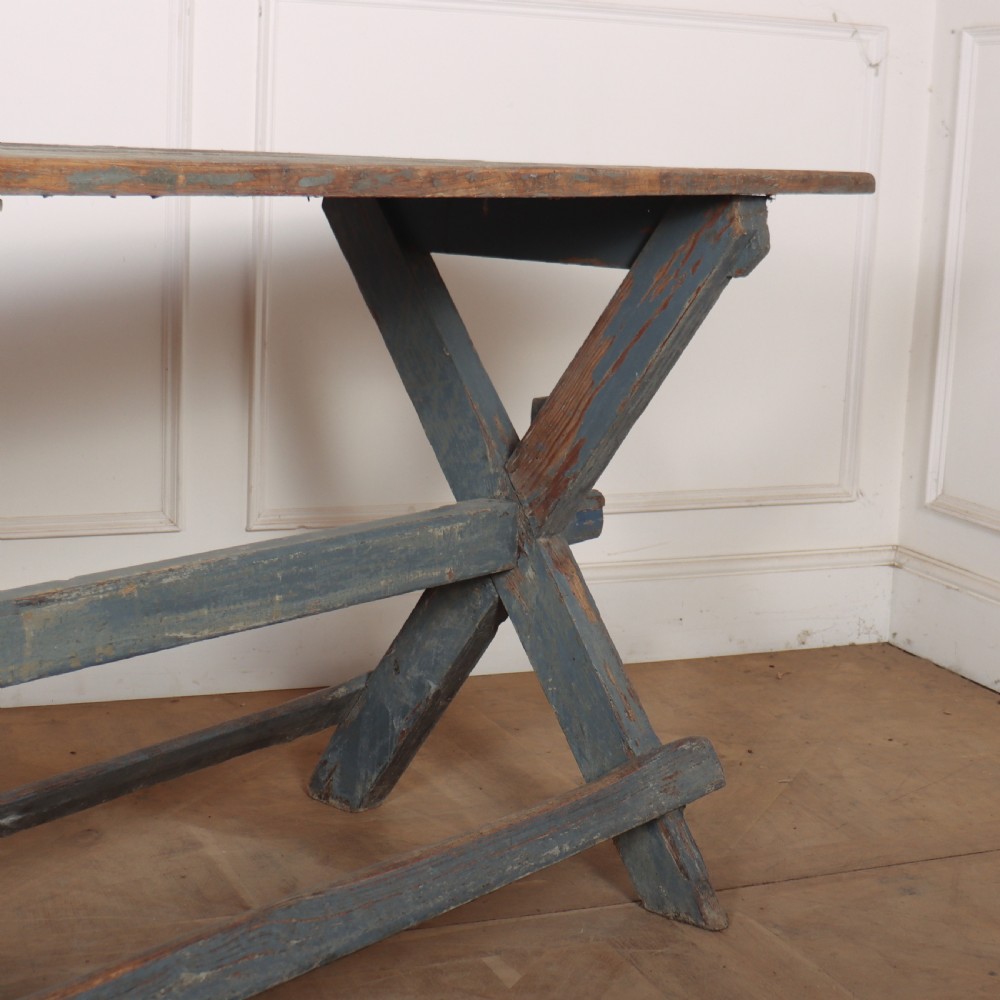 A long antique wooden tavern table with a natural wood plank top and a blue-painted X-frame trestle base. View IV