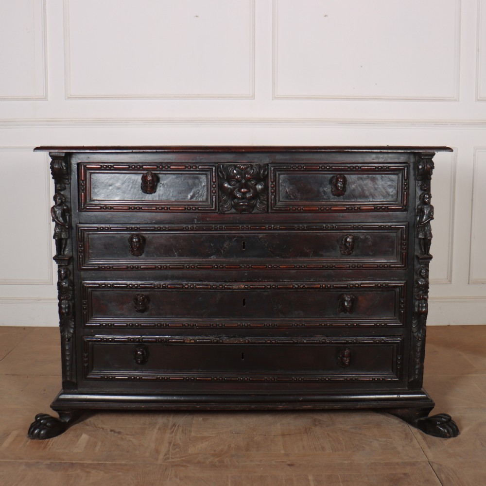 An 18th-century dark walnut Italian commode featuring carved mask pulls, caryatid pilasters, and carved claw feet.