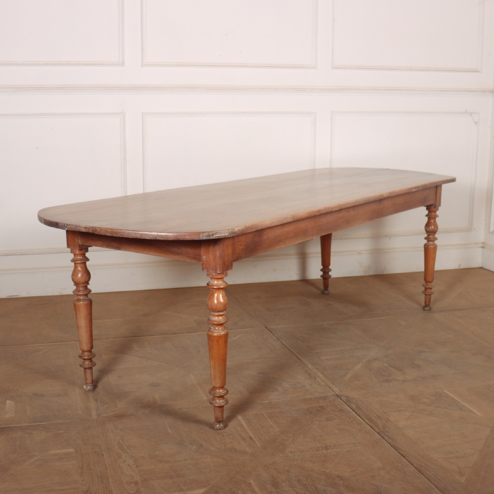 A long wooden French farmhouse dining table featuring rounded D-shaped ends and turned legs.