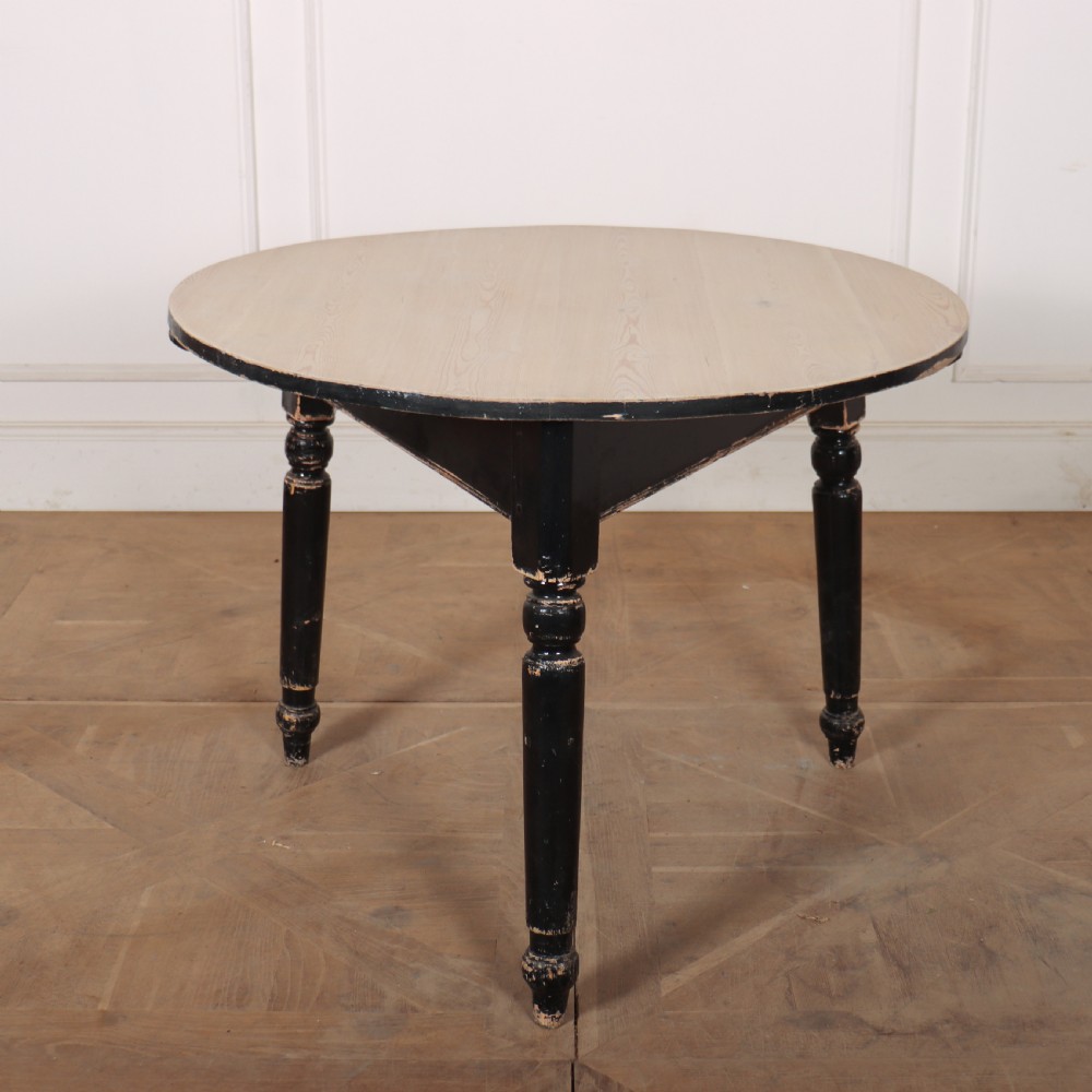 A Welsh pine cricket table featuring a circular scrubbed timber top supported by three turned legs in a distressed black painted finish.