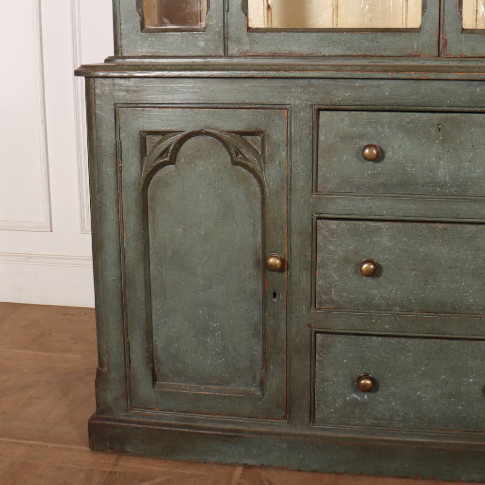 A two-part blue-green painted timber dresser featuring an upper glazed cabinet with gothic arch doors and a lower base fitted with drawers and cupboard doors. View II