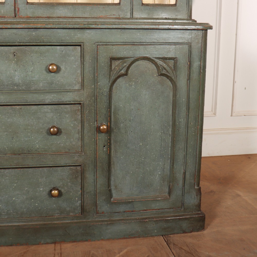 A two-part blue-green painted timber dresser featuring an upper glazed cabinet with gothic arch doors and a lower base fitted with drawers and cupboard doors. View III