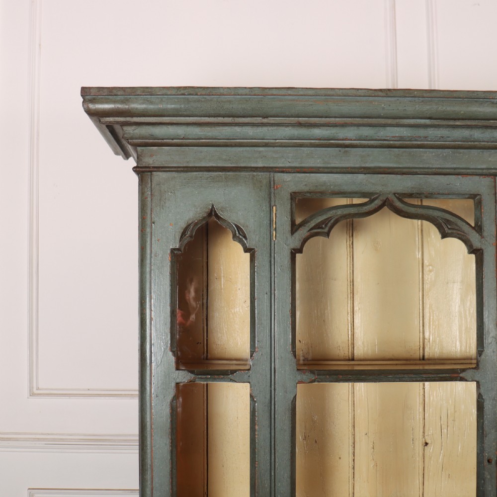 A two-part blue-green painted timber dresser featuring an upper glazed cabinet with gothic arch doors and a lower base fitted with drawers and cupboard doors. View V