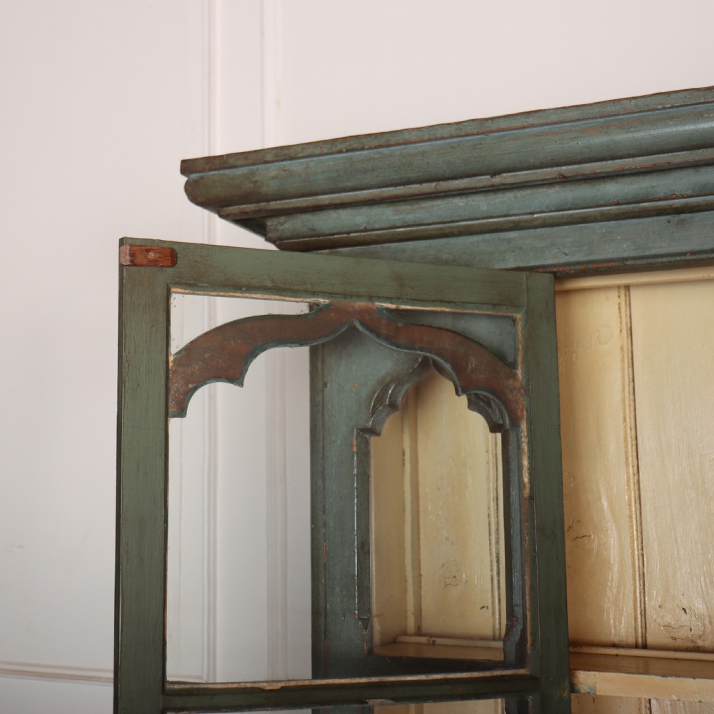 A two-part blue-green painted timber dresser featuring an upper glazed cabinet with gothic arch doors and a lower base fitted with drawers and cupboard doors. View VII
