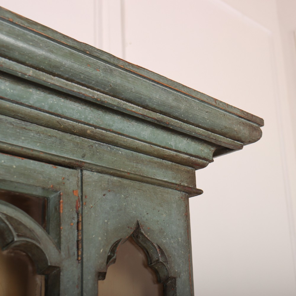A two-part blue-green painted timber dresser featuring an upper glazed cabinet with gothic arch doors and a lower base fitted with drawers and cupboard doors. View IX