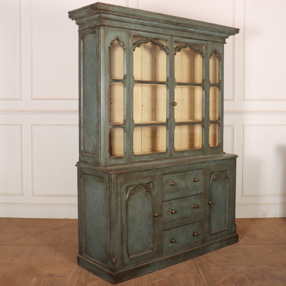 A two-part blue-green painted timber dresser featuring an upper glazed cabinet with gothic arch doors and a lower base fitted with drawers and cupboard doors. View XI
